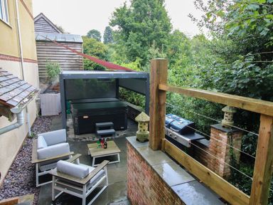 An outdoor patio area with seating a hot tub a barbecue and trees at Sunnyside in Bircher Common near Yarpole