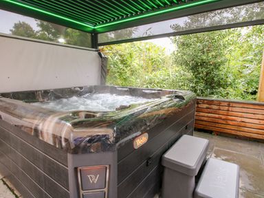 An outdoor hot tub with steps under a covered area surrounded by greenery at Sunnyside in Bircher Common near Yarpole