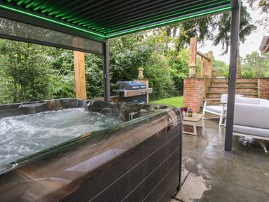 An outdoor covered patio with a hot tub a barbecue grill and seating area with chairs and a table at Sunnyside in Bircher Common near Yarpole
