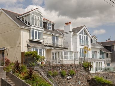 A row of multi-story houses with balconies and large windows overlooking a stone wall with plants at Seascape in Salcombe