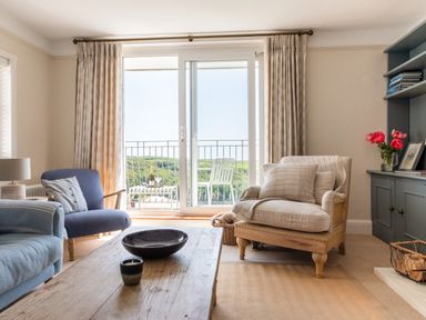 A living room with chairs a wooden coffee table a bookshelf and a balcony door at Seascape in Salcombe