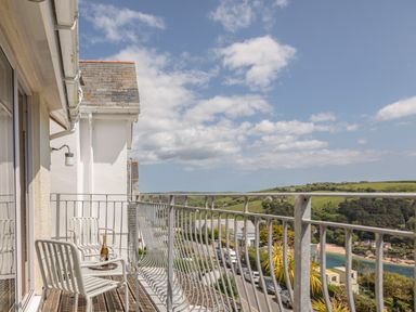 A balcony with two metal chairs a bottle and glasses overlooking a coastal town and green hills at Seascape in Salcombe