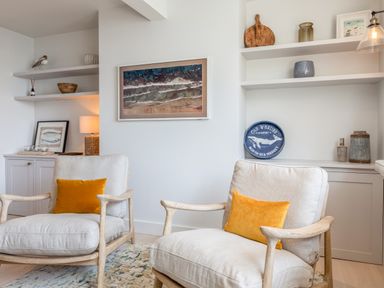 Two armchairs with yellow cushions in a room with white walls and built-in shelves at Seascape in Salcombe