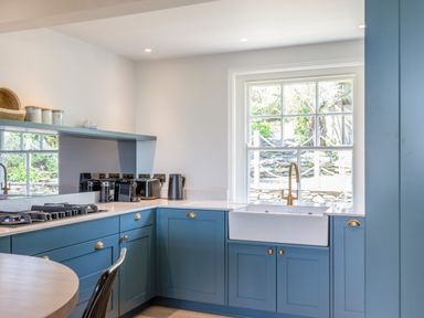 A kitchen with blue cabinets a white sink a gas stove and a window showing a stone wall and plants at Seascape in Salcombe