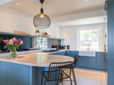 A kitchen with blue cabinets a wooden island two black chairs and a window at Seascape in Salcombe
