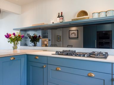 A kitchen with blue cabinets a gas stove a bouquet of flowers in a glass vase and a shelf with jars and bottles at Seascape in Salcombe