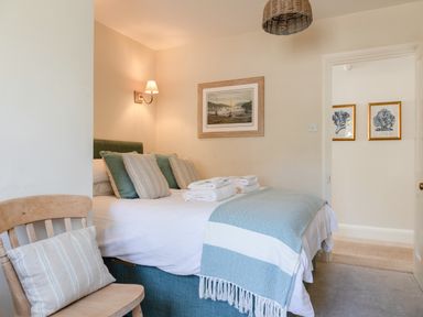 A bedroom with a bed with pillows and folded towels next to a wooden chair with a cushion at Seascape in Salcombe
