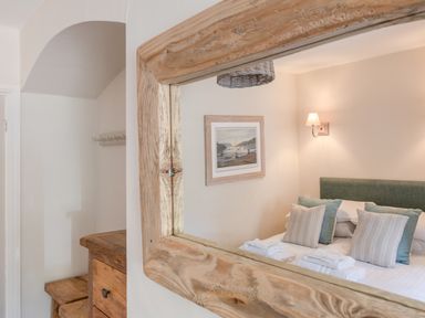 A mirror reflecting a bedroom with bed pillows wall lamp and framed picture at Seascape in Salcombe