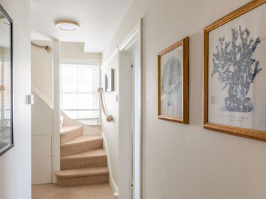 A hallway with carpeted stairs leading up and framed pictures on the wall at Seascape in Salcombe