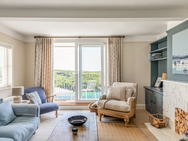 A living room with sofa armchairs coffee table and a fireplace with wood at Seascape in Salcombe