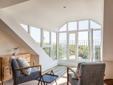 A room with two chairs a wooden dresser and large windows overlooking a coastal landscape at Seascape in Salcombe