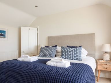 A bedroom with a bed covered in a blue textured blanket with folded white towels on top and two bedside tables with lamps at Seascape in Salcombe
