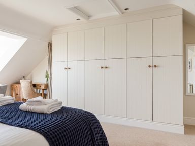 A bedroom with folded towels on a bed a large white wardrobe and a wooden desk with a chair at Seascape in Salcombe