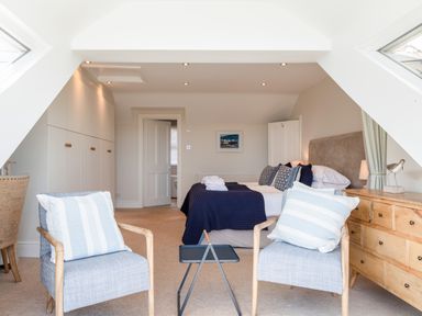 A bedroom with two armchairs and a small table in front of a double bed at Seascape in Salcombe