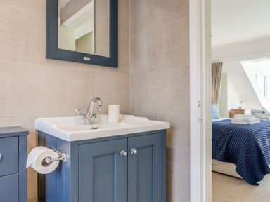 A bathroom sink with blue cabinets and a mirror above next to a bedroom with a bed covered in a blue blanket at Seascape in Salcombe