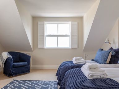 A bedroom with twin beds, blue bedding, a blue armchair, and a window with white shutters at Seascape in Salcombe