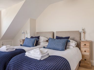 A bedroom with two single beds with blue pillows and throws and wooden bedside tables with lamps at Seascape in Salcombe
