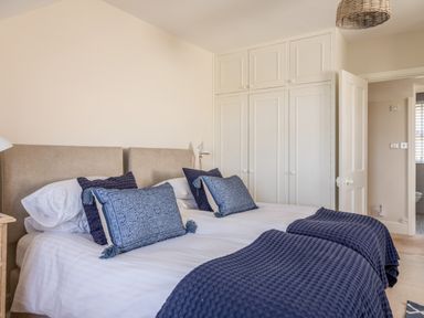A bedroom with two single beds joined with blue pillows and blankets and white built-in wardrobes at Seascape in Salcombe