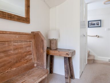 A hallway with a wooden bench wooden table with a lamp a framed picture and carpeted stairs at Seascape in Salcombe