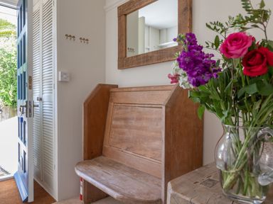 An entryway with a wooden bench a mirror a bouquet of flowers in a glass vase and an open blue door at Seascape in Salcombe