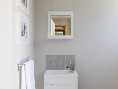A bathroom sink with a faucet and gray tile backsplash below a mirror and two framed pictures on the wall at Seascape in Salcombe