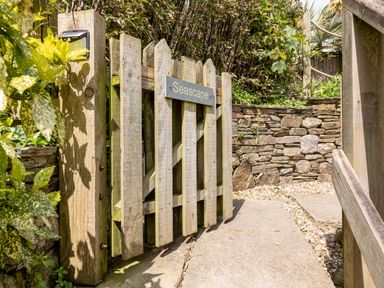 A wooden gate with a Seascape sign near a stone wall and plants at Seascape in Salcombe