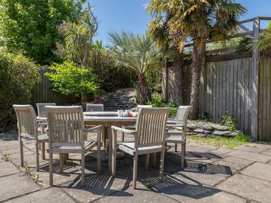 An outdoor patio area with a round wooden table and six wooden chairs surrounded by plants and a wooden fence at Seascape Salcombe