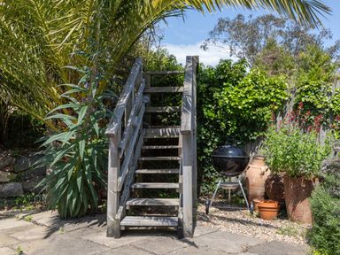A wooden staircase in a garden with plants pots and a charcoal grill near a fence at Seascape in Salcombe