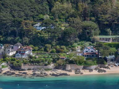 A coastal area with houses surrounded by trees and gardens next to a beach with rocks at Seascape in Salcombe