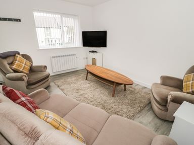 A living room with a sofa and armchairs around a wooden coffee table and a wall-mounted television at Trigfa in Llanfechell