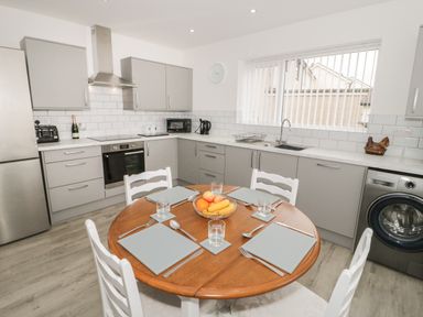 A kitchen with gray cabinets a round wooden dining table set for four and a washing machine under the counter at Trigfa in Llanfechell