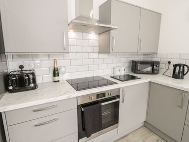 A kitchen with grey cabinets a black toaster a bottle and glass a stovetop an oven a microwave and a kettle at Trigfa in Llanfechell