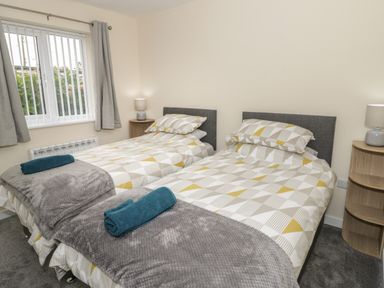 A bedroom with two single beds with patterned bedding and blue towels on grey blankets at Trigfa in Llanfechell
