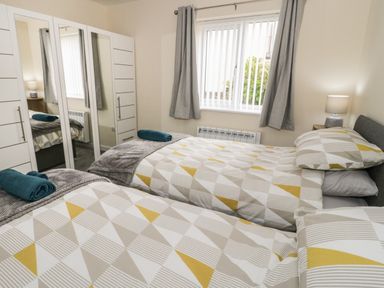 A bedroom with two single beds a wardrobe with mirrors and a window with curtains at Trigfa in Llanfechell