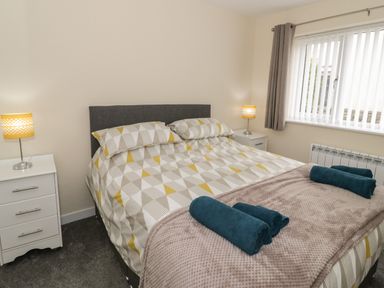 A bedroom with a double bed bedside tables with lamps and a window with vertical blinds at Trigfa in Llanfechell