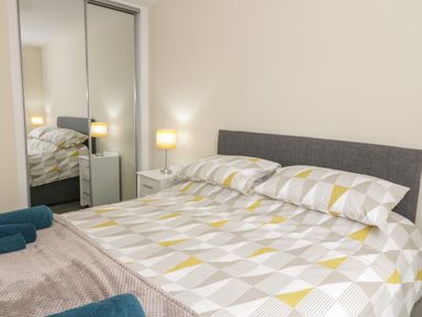 A bedroom with a double bed bedside tables with lamps and mirrored sliding wardrobe doors at Trigfa in Llanfechell