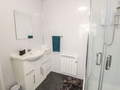 A bathroom with a white sink cabinet mirror towel heater shower and floor mat at Trigfa in Llanfechell