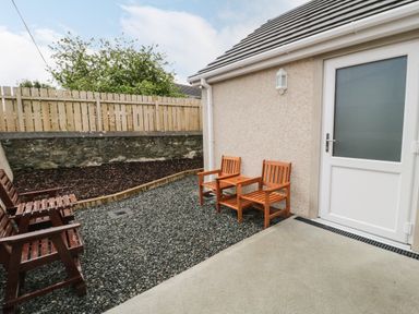 A small outdoor patio area with wooden chairs and a table near a door at Trigfa in Llanfechell