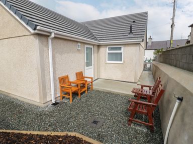A gravel courtyard with four wooden chairs outside a beige building at Trigfa in Llanfechell