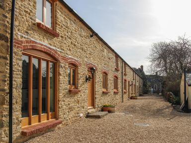 A stone building with wooden windows and doors along a gravel pathway at The Granary Burton Bradstock