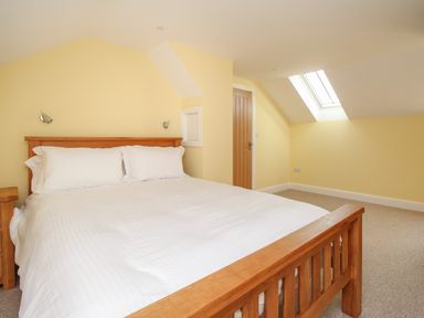 A bedroom with a wooden bed and white bedding near a wooden door and skylight at The Granary Burton Bradstock