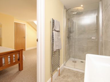 A bathroom with a glass shower enclosure and towel rack next to a bedroom with a wooden bedframe at The Granary Burton Bradstock