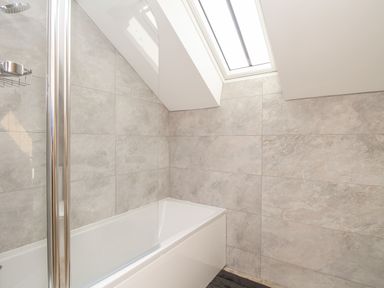 A bathroom with a bathtub and tiled walls and a skylight window at The Granary Burton Bradstock