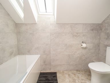 A bathroom with a bathtub a toilet a toilet paper holder and a black bath mat on the floor at The Granary Burton Bradstock