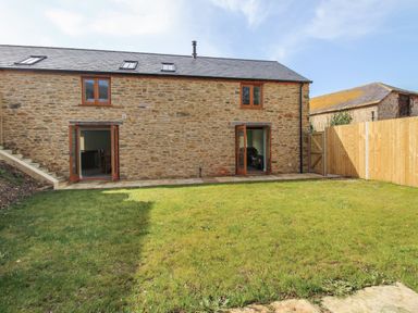 A stone house with two wooden framed windows and two open wooden framed doors opening to a lawn with a wooden fence and stone steps on the left at The Granary Burton Bradstock