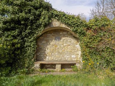 A stone garden bench with a curved stone wall and ivy growing around it at The Granary Burton Bradstock
