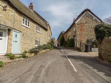 A narrow street with stone cottages on both sides and plants along the houses at The Granary Burton Bradstock