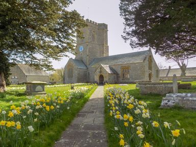 A stone church with a clock tower surrounded by daffodils and gravestones