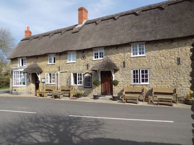 A stone building with thatched roof benches and potted plants outside at The Granary Burton Bradstock