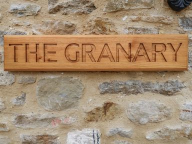 A wooden sign with the words THE GRANARY carved into it mounted on a stone wall at The Granary Burton Bradstock
